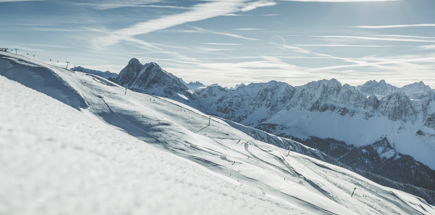 Das Bild zeigt das Skigebiet Plose. auf über 2.000 m. Hier liegt genug Schnee und im Hintergrund zeigen sich königlich die Geisler-Dolomiten von Afers und Villnöss.