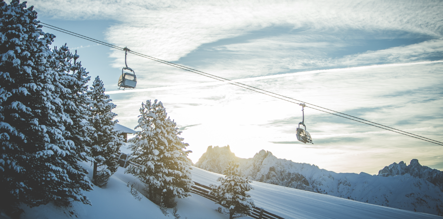 Almgasthof Geisler | Sciare e trascorrere le vacanze invernali sulla Plose è la decisione migliore, perché a 2.000 m c'è abbastanza neve! L'immagine mostra una seggiovia e conifere innevate con rami sani e distesi. Sullo sfondo le montagne innevate dell'Alto Adige.