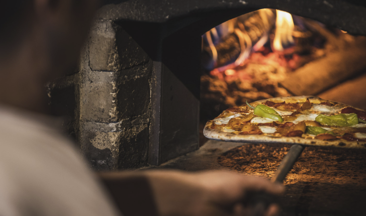 Almgasthof Geisler | Puro piacere della pizza per tutto l'inverno, direttamente sulla Plose sopra Bressanone. La foto mostra il pizzaiolo mentre prende una pizza Diavola con salame piccante e peperoncini dal forno a legna. L'impasto è fatto a mano.